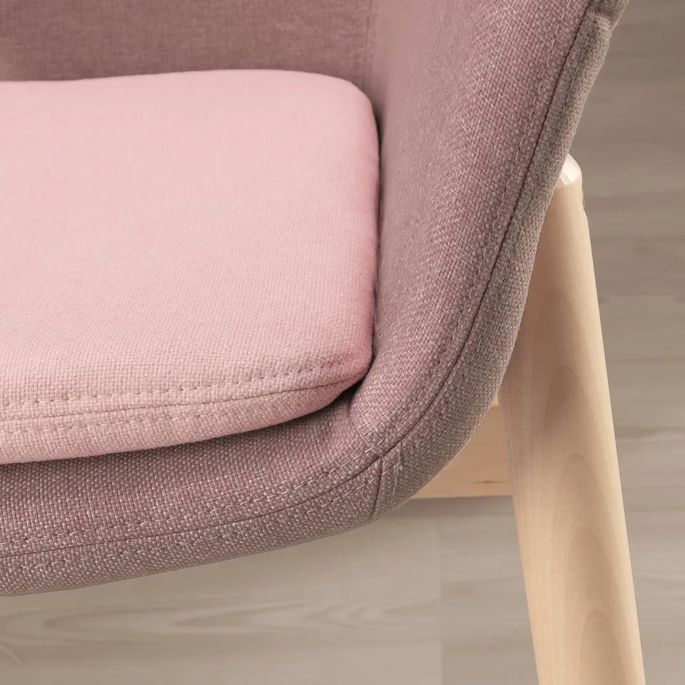 Close-up of a pink upholstered armchair, showcasing its soft, curved lines and sturdy wooden leg.