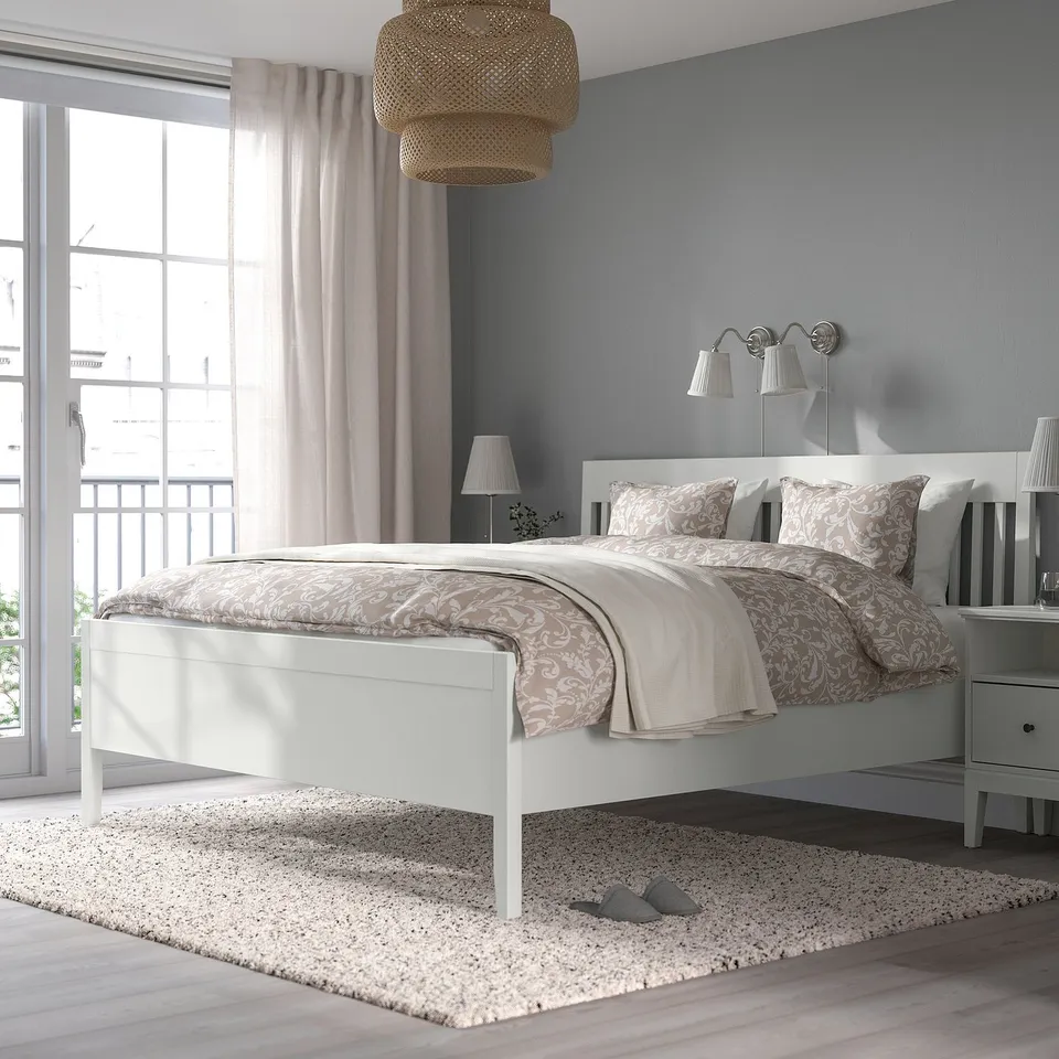 Minimalist bedroom with IDANÄS white bed, patterned beige bedding, large window, light grey curtains, and hanging lamps.