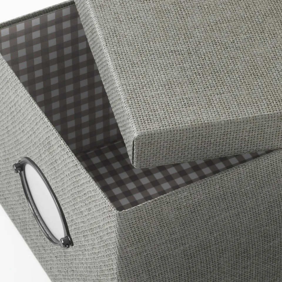 A grey KVARNVIK storage box with a woven texture and chequered interior lining. It a round handle on the side.