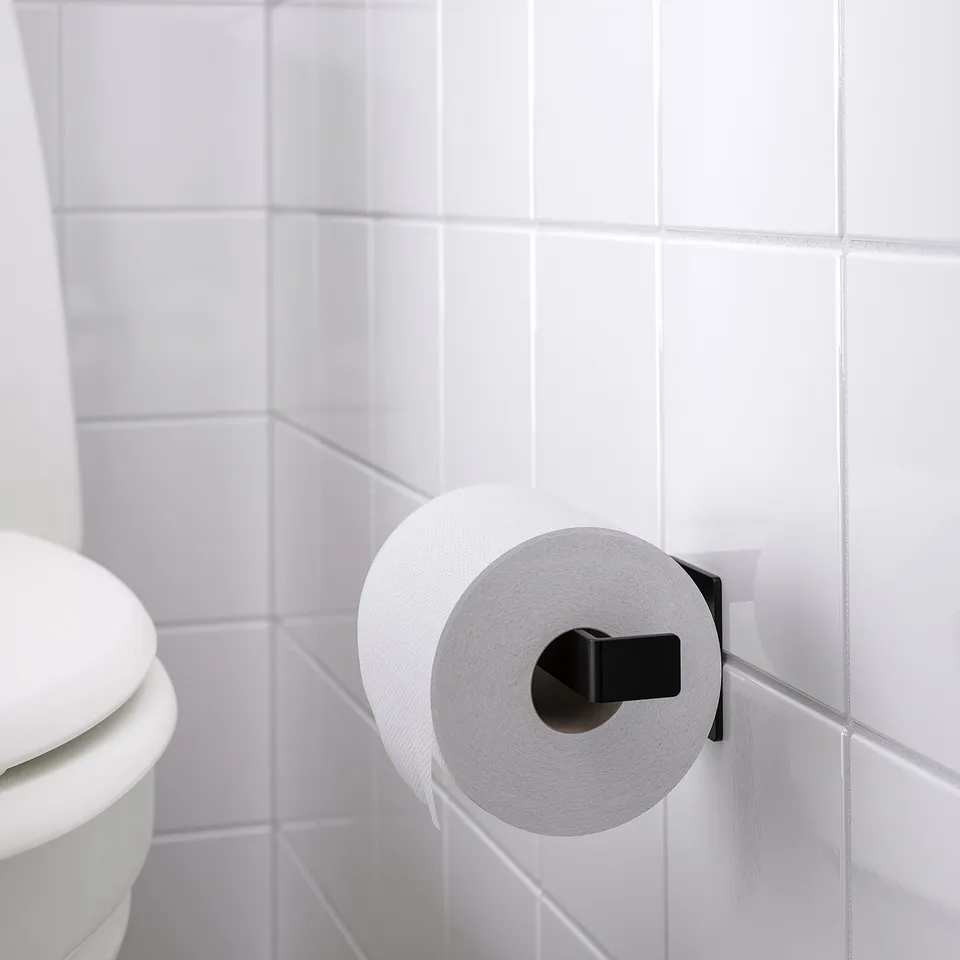 Black toilet paper holder mounted on white tiled wall, holding a roll of white toilet paper.