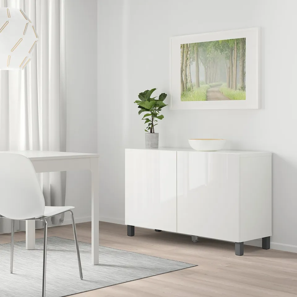 Modern living space with STUBBARP dark grey legs on white bestå cabinet, plant, bowl, white table, chair, green forest art.