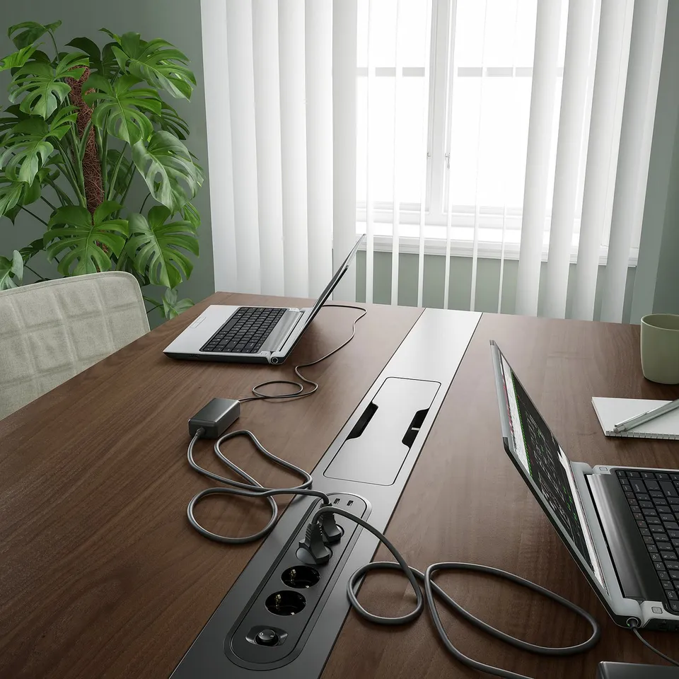 Conference table with laptops, extension cords, and plant, ideal for meetings and co-working.
