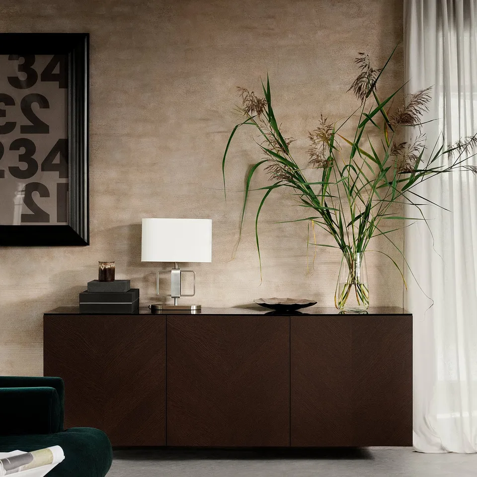 Modern living room with dark brown BESTÅ cabinet, green chair, white lamp, tall plant in glass vase, and framed artwork on textured wall.