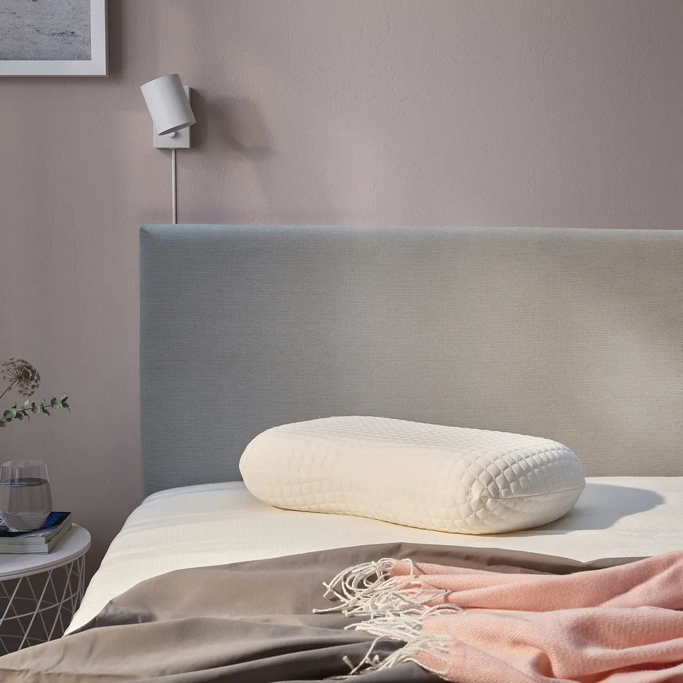 Modern bedroom with NORDSTÅLÖRT pillow on bed, glass on bedside table.