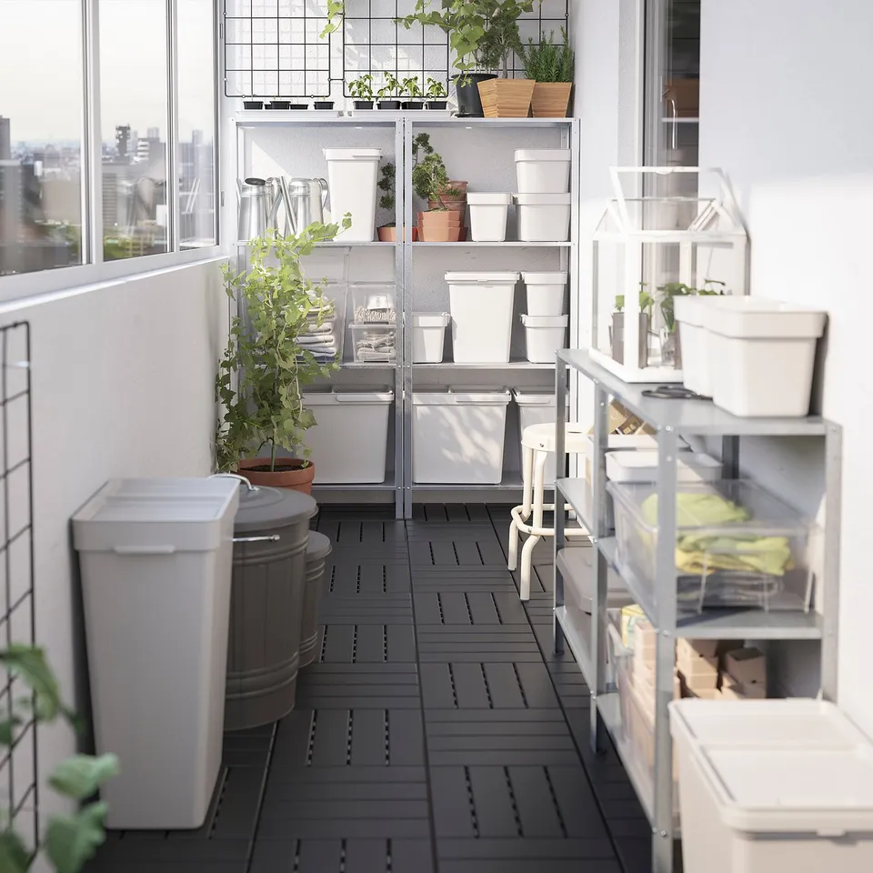 Balcony garden with white metal shelves, potted plants, and HÅLLBAR recycling bins.