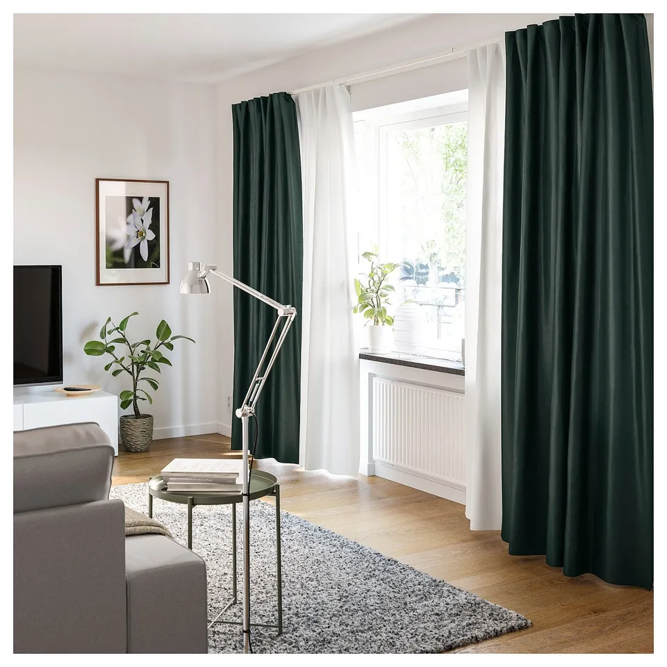 Modern living room with grey sofa, wooden floor, VIDGA dark green curtains, white lamp, plants, and tv.