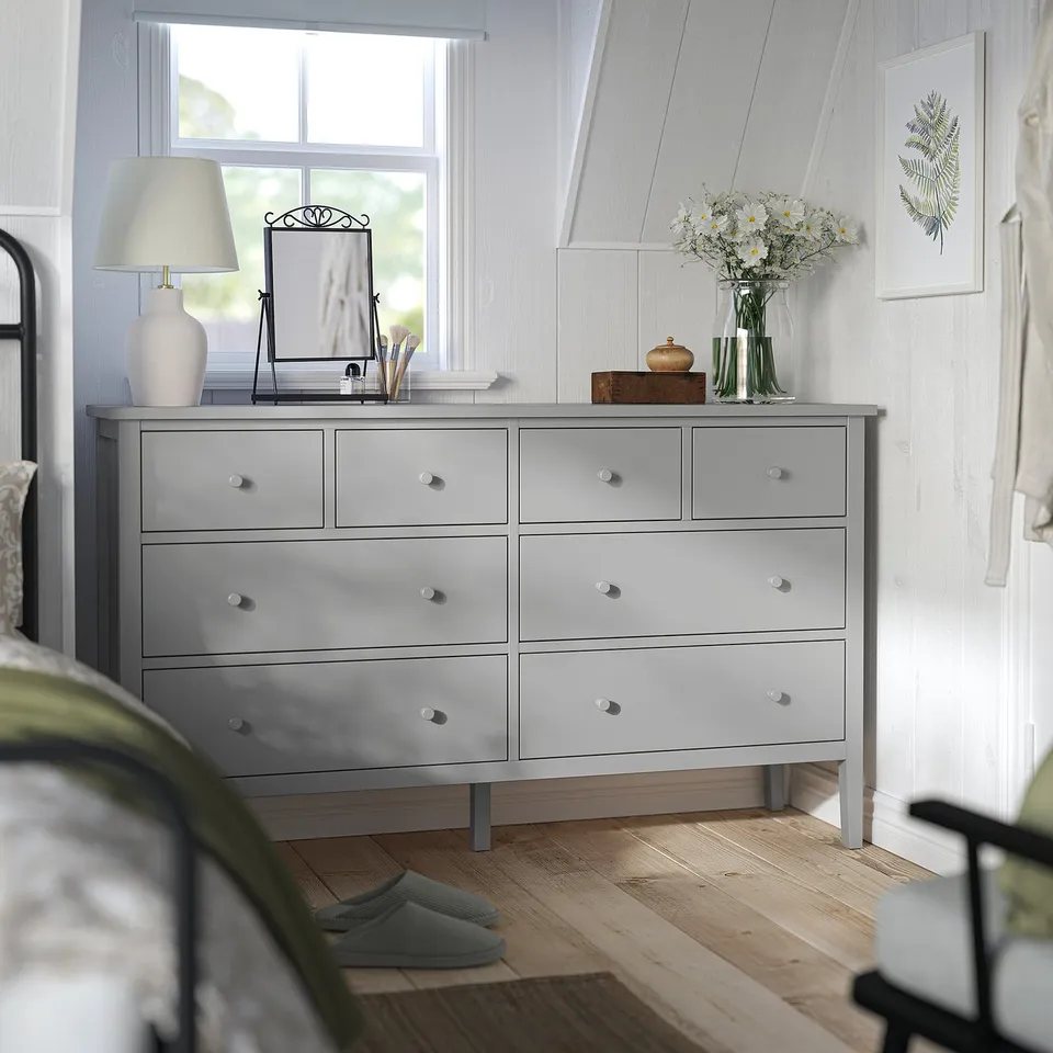 A cosy bedroom featuring a light grey GULLABERG 8-drawer chest, adorned with flowers, under a window.
