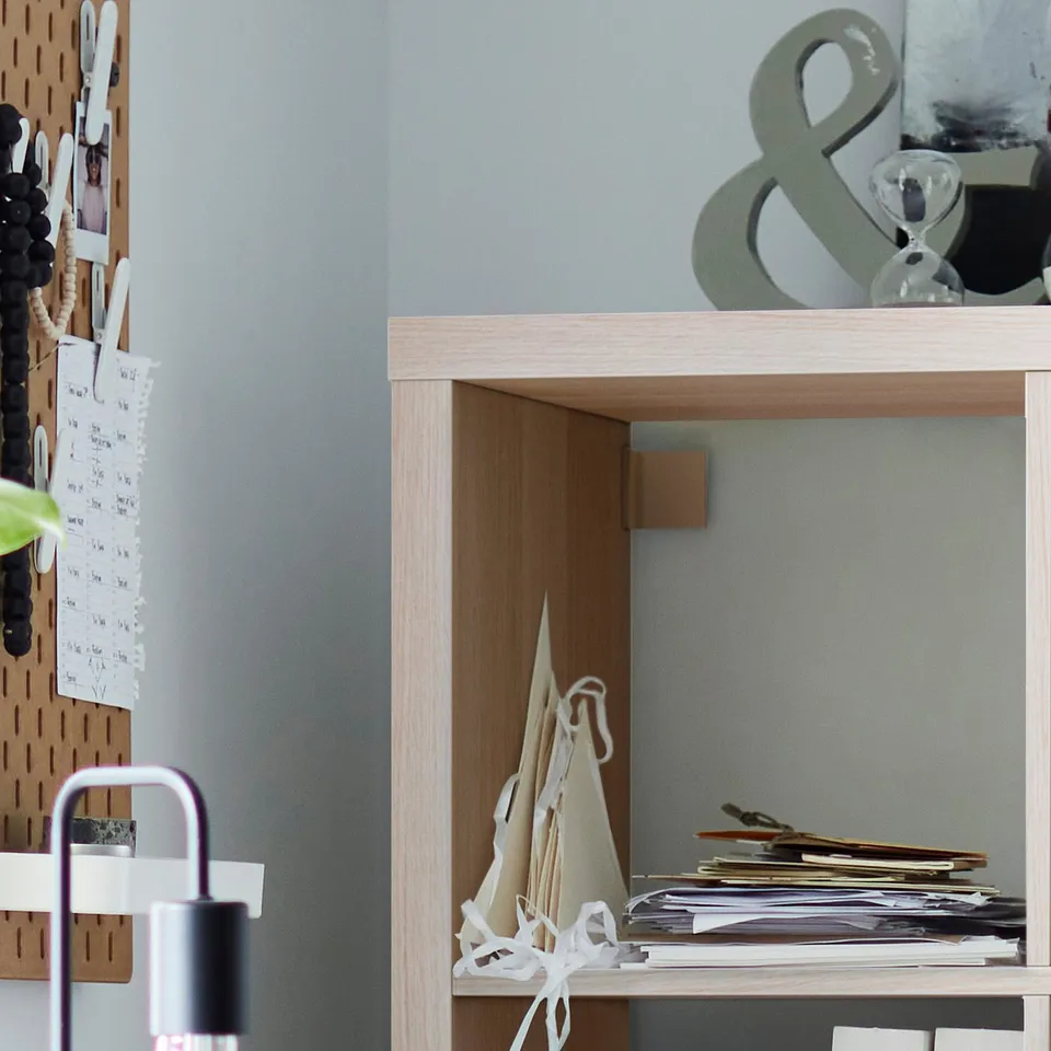 Light wooden KALLAX shelving unit with papers and a lamp.
