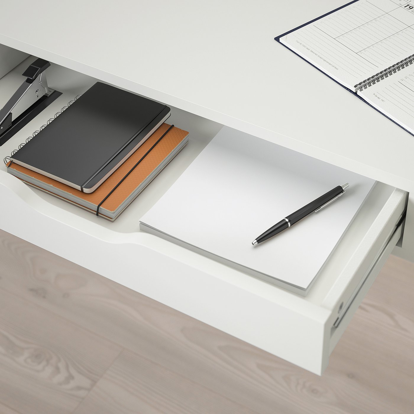 A white wall-mounted desk with a notebook, pen, and another notebook on shelves.