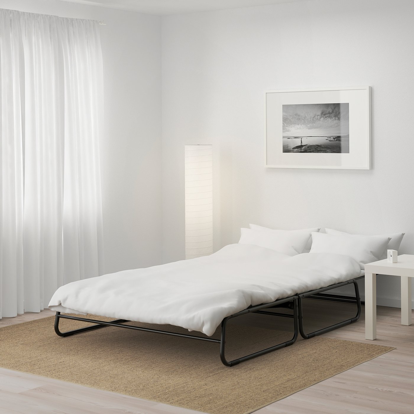A modern bed in a minimalist room with white bedding, a side table, and a framed photo on the wall.
