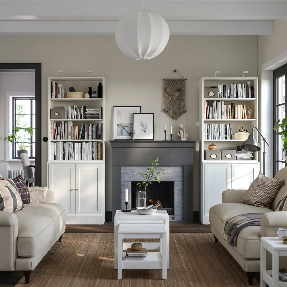 Modern living room with HAVSTA white pine bookcases, beige couches, and a grey fireplace. Decorative lighting and natural decor elements.