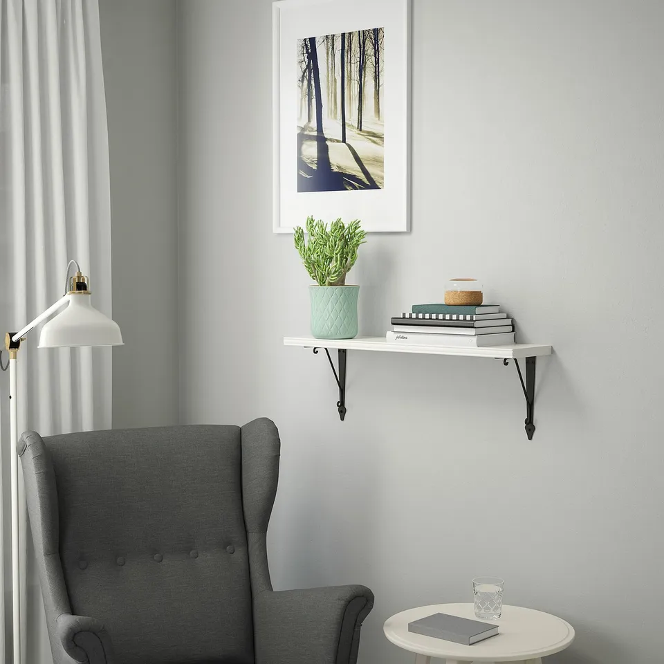 Modern living space with BERGSHULT shelf holding books, plant, decor, grey armchair, and table with glass and notepad.