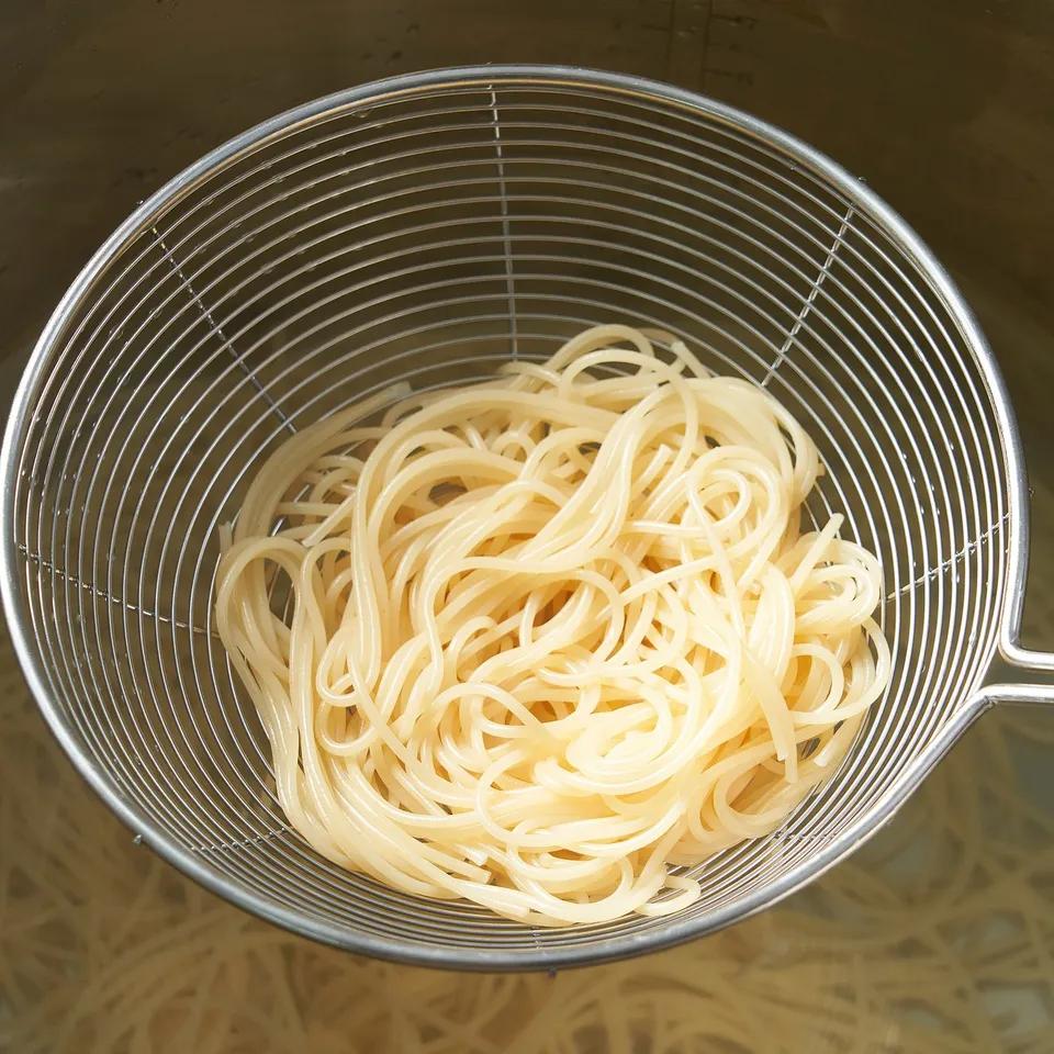Metal colander filled with cooked noodles, showing its draining function. Handle on side for easy use.