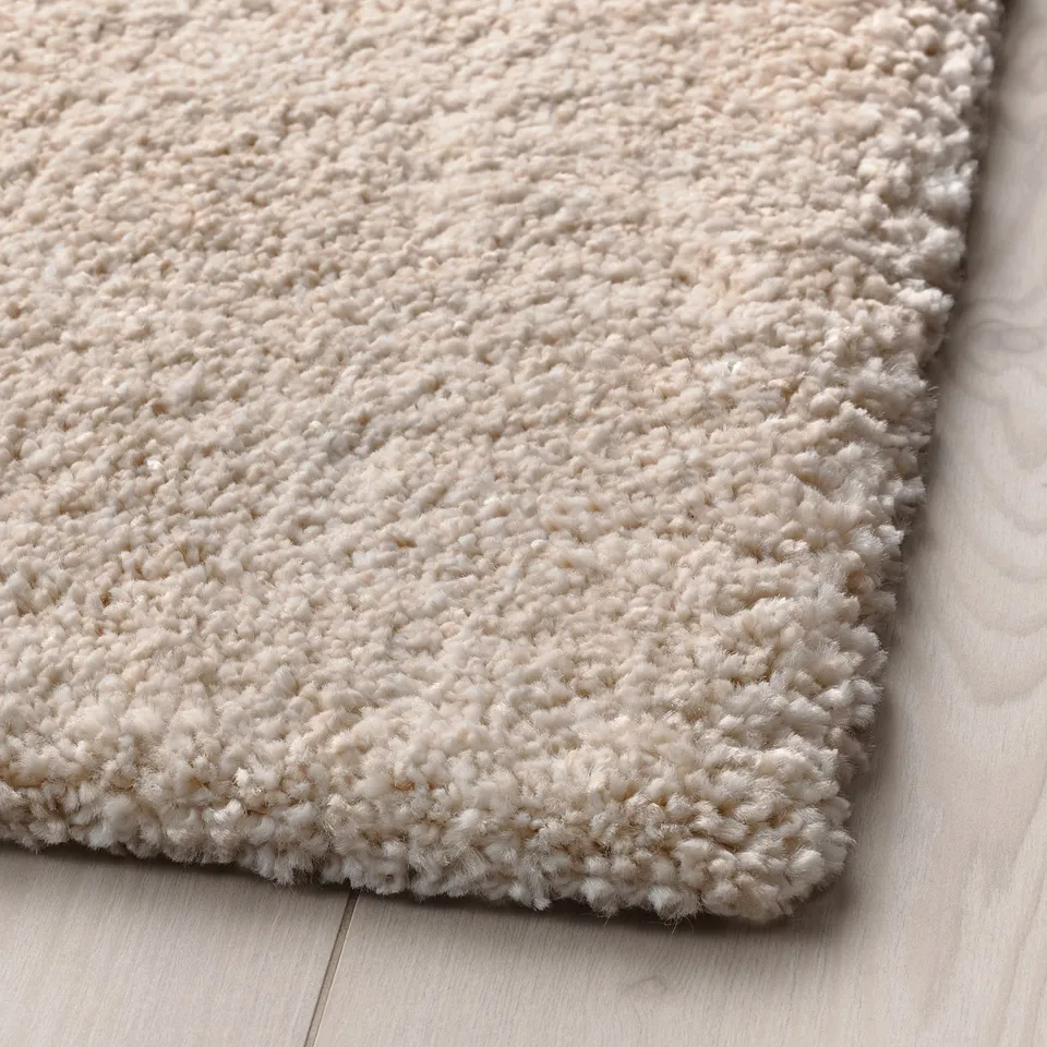Plush, cream rug on light wood floor, inviting with shiny finish.