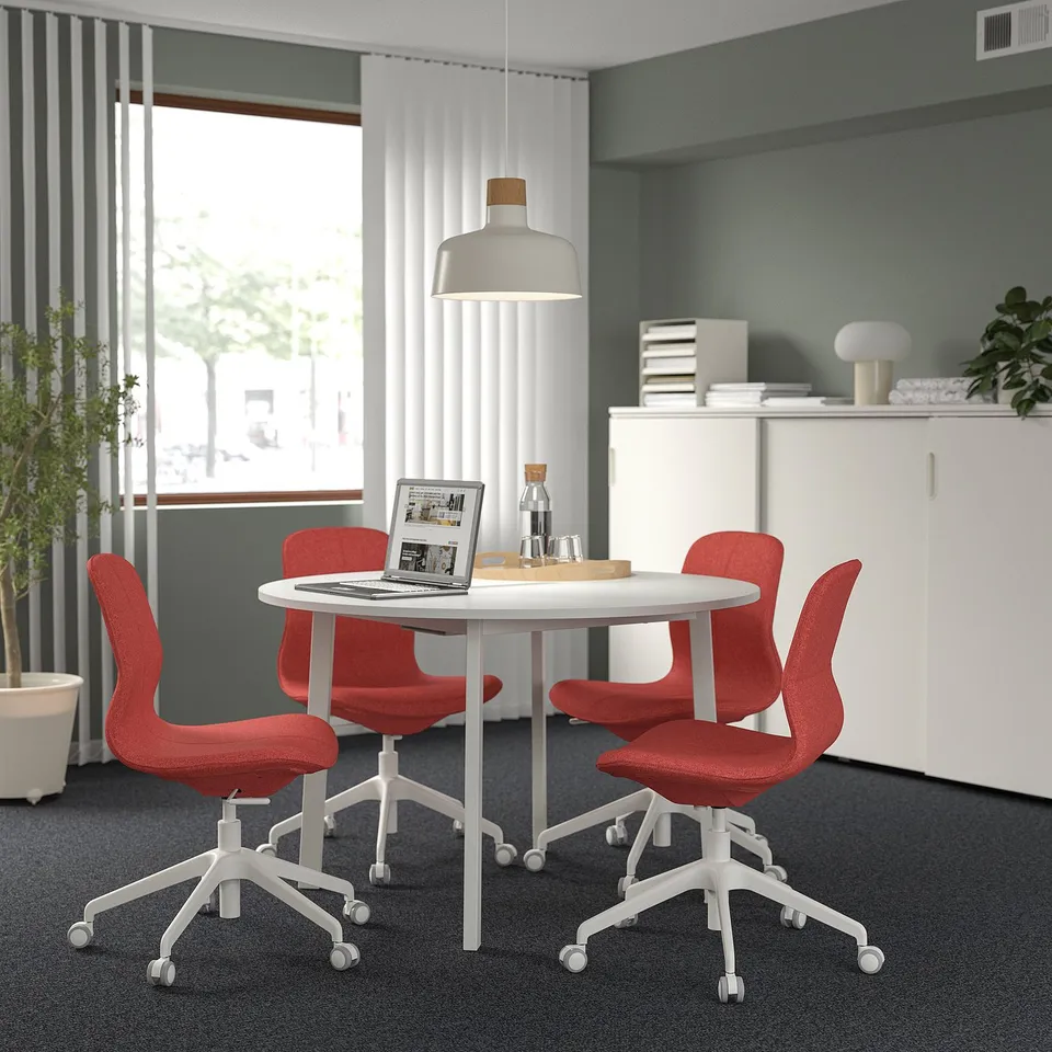 Modern office with round MITTZON table, red chairs, large window, and white cabinet.