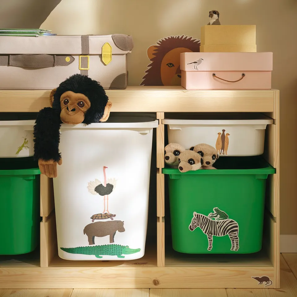 Childs storage bins with savannah-themed stickers: zebra, giraffe, hippo, flamingo, and baby chimpanzee, arranged neatly on wooden shelves.