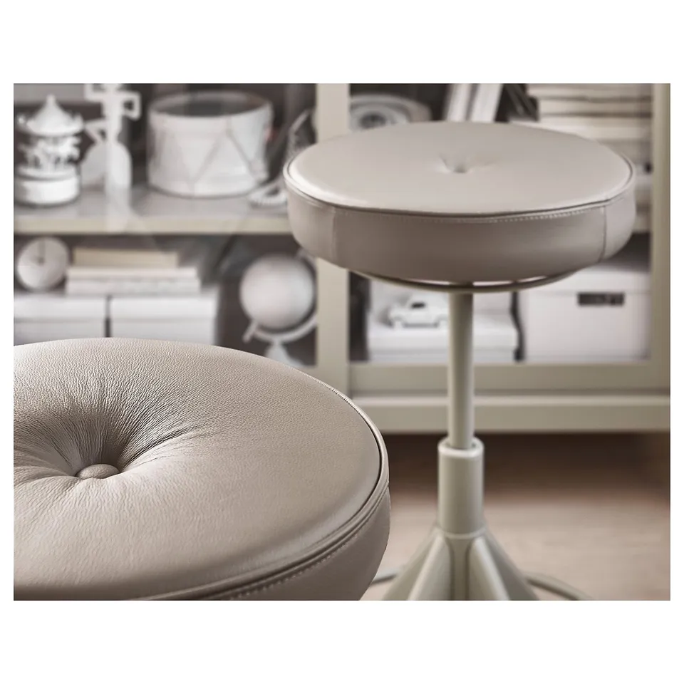 Image two beige leather round stools, one with a star base, placed before a shelf with decorative items.