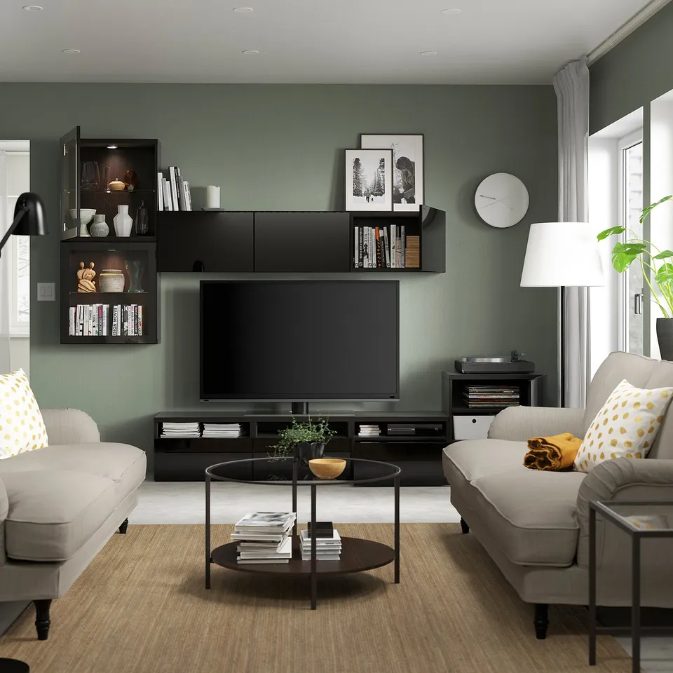 Modern living room with grey sofa, coffee table, large tv on dark wood stand, wall-mounted shelves with books and decor, and a round black floor lamp.