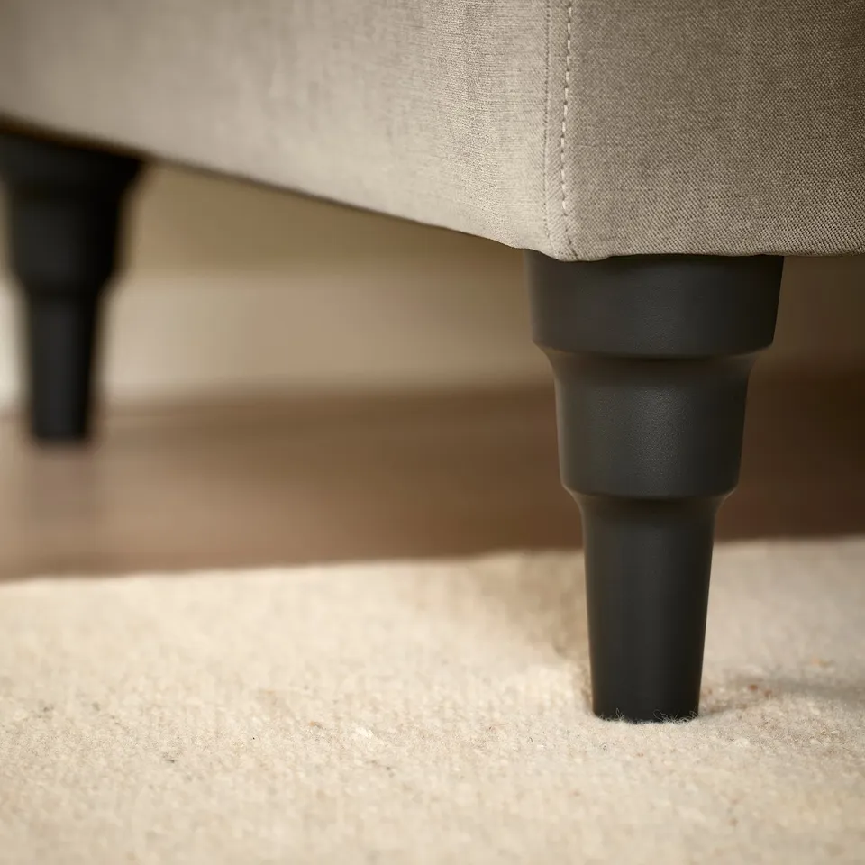 Close-up of beige sofa legs, modern design, sturdy black plastic support.