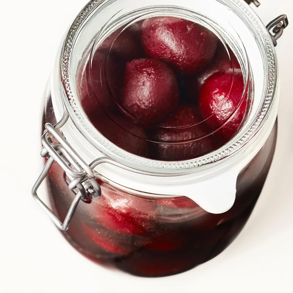 Glass jar with metal lid, holding dark red liquid and plums for preservation.