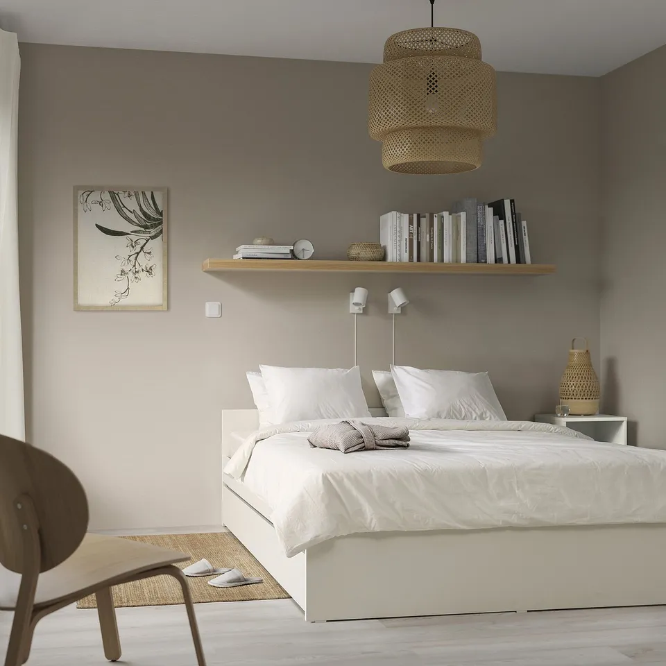 Modern bedroom with white VIHALS bed, neatly made. Grey wall, wooden shelf, pendant light, chair, and side table. Minimalist and elegant design.