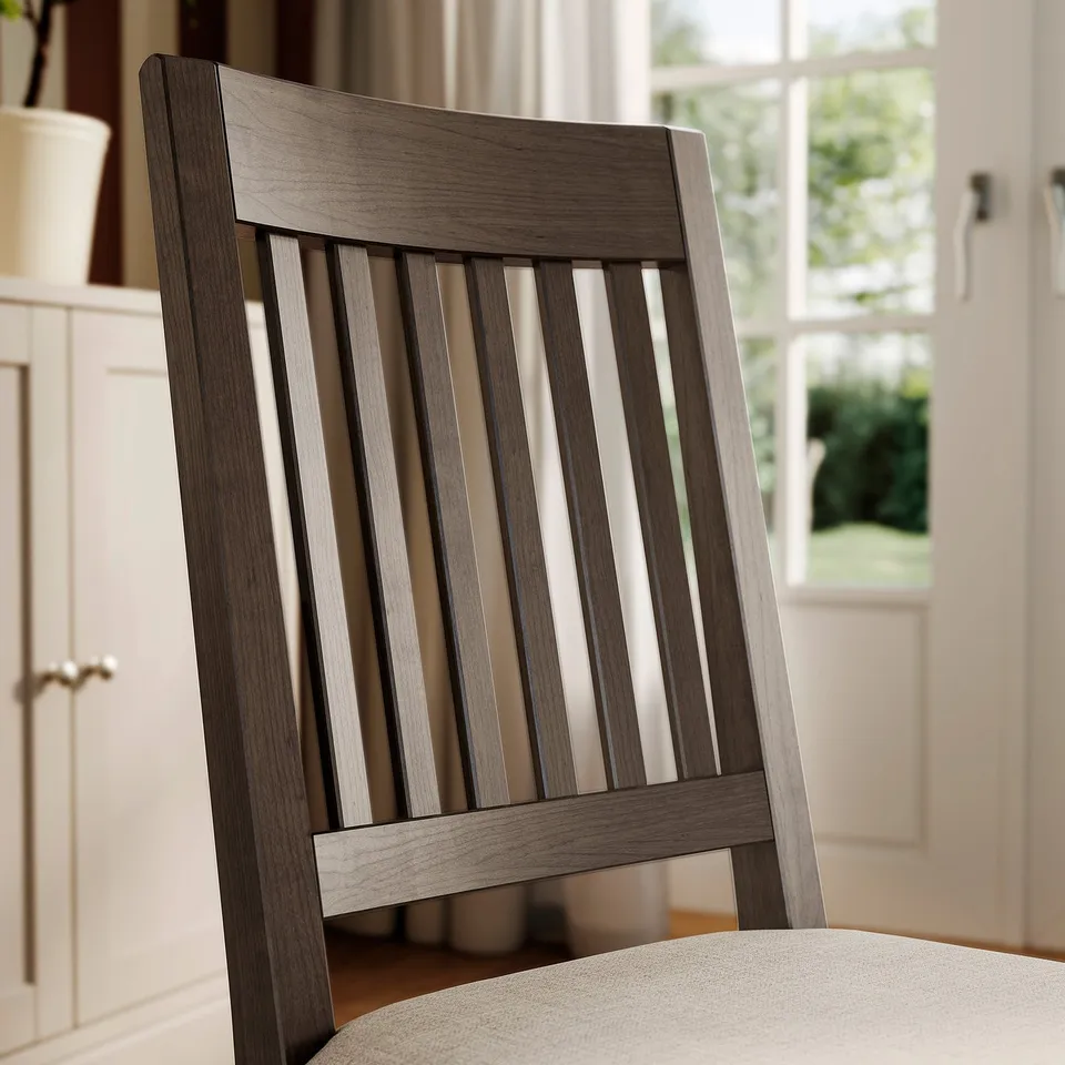 A modern wooden chair with a slatted back and beige cushion, set in a bright room.