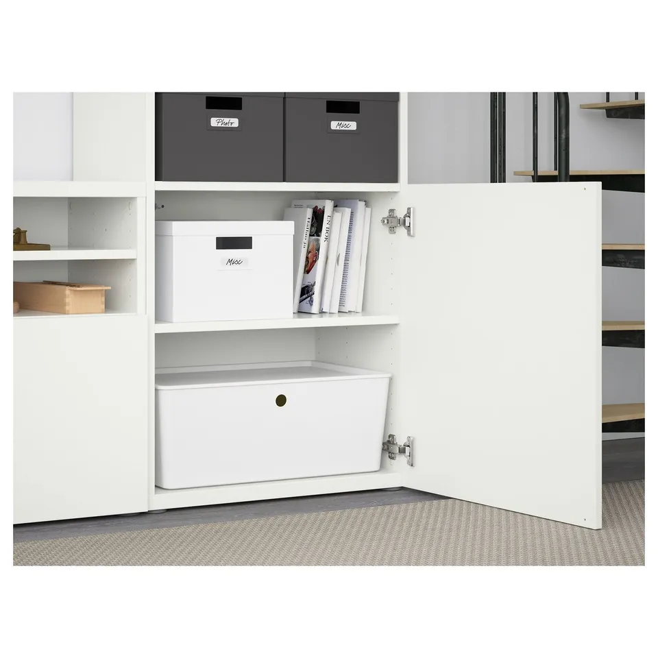 White BESTÅ shelf unit with adjustable shelves, boxes, and open compartments. The door is open, revealing a drawer and storage space.