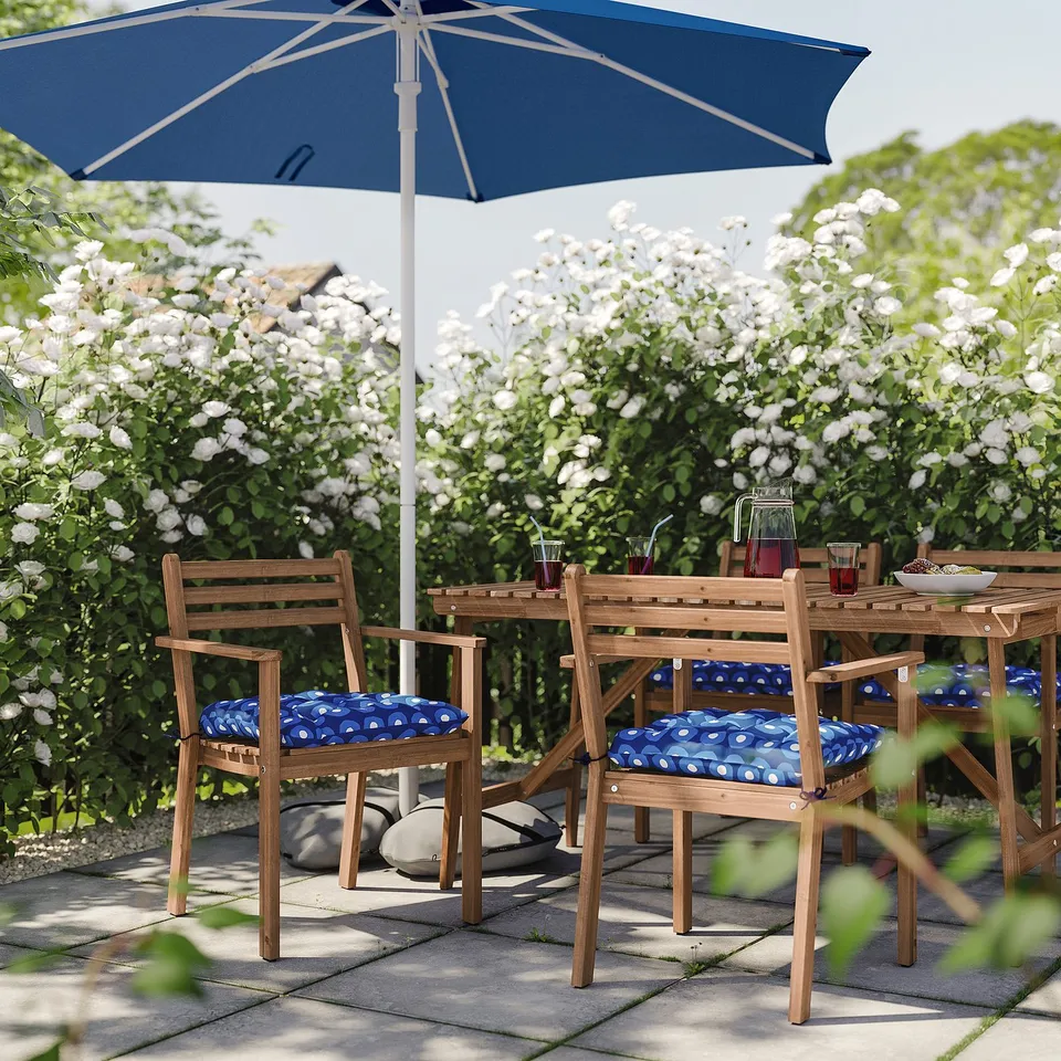 Outdoor patio set with blue chairs, wooden table, blue umbrella, and white flower backdrop.