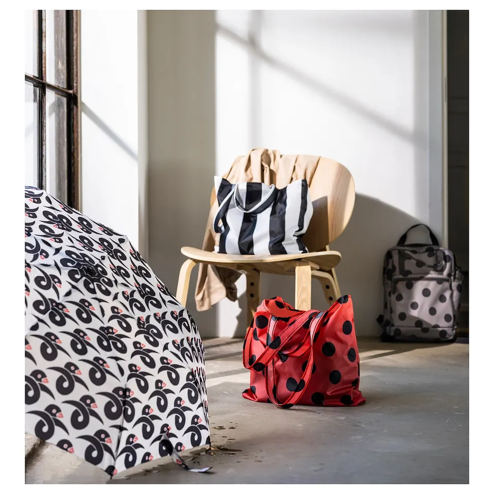 Four colourful SKYNKE bags shown indoors, two on floor, one on chair, one near windows. Lightweight, foldable, 100% recycled polyester.