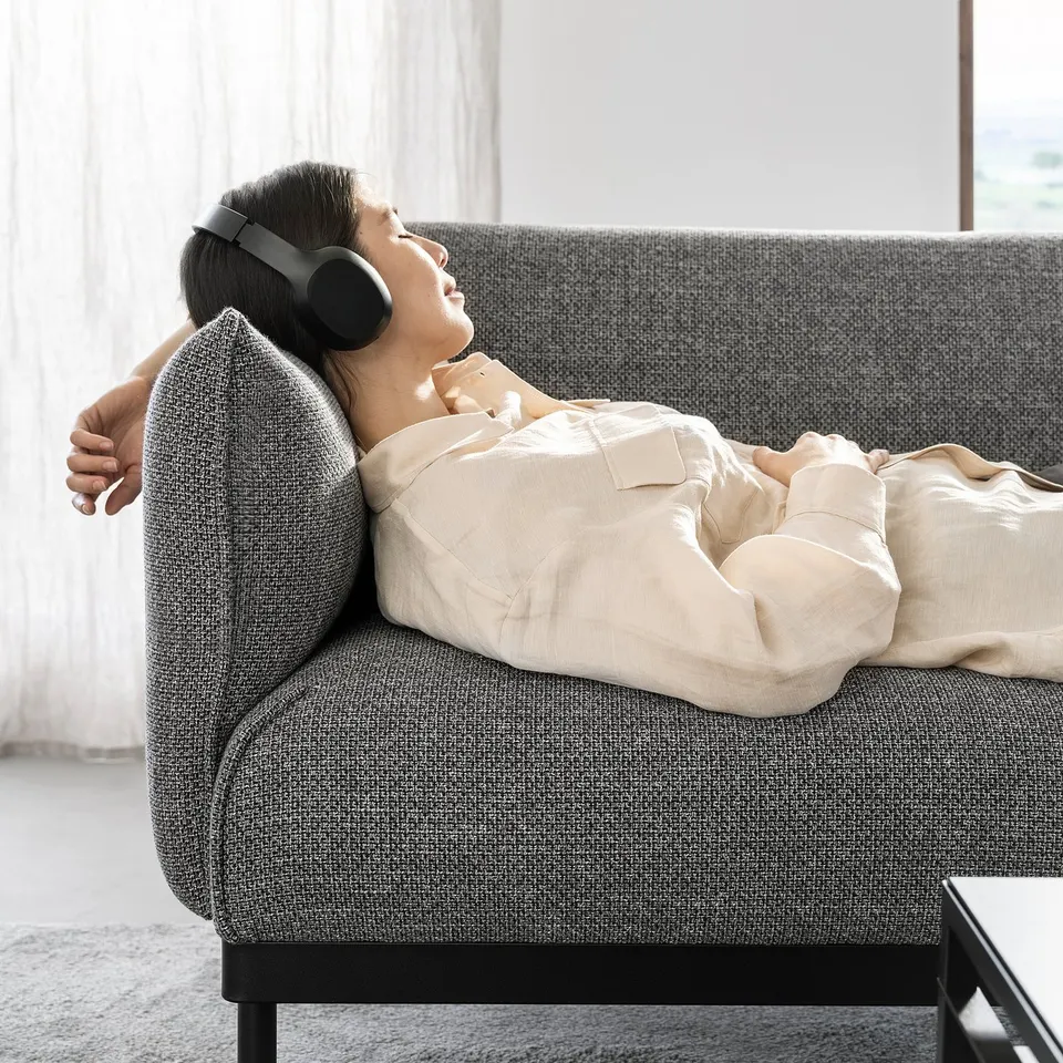 Person relaxing on grey ÄPPLARYD sofa, wearing headphones, comfortable in beige outfit.