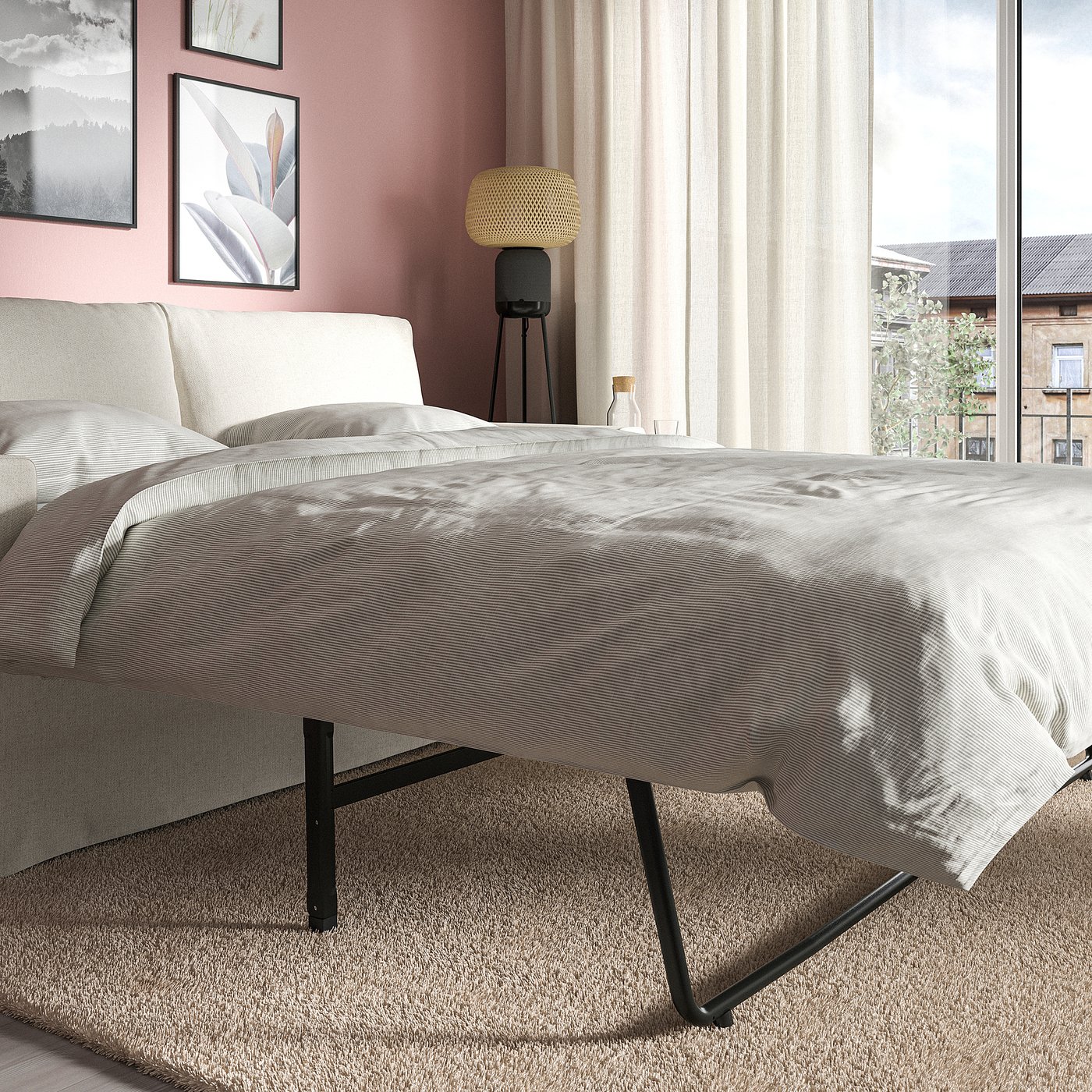 Bed transformed from sofa, showing large cushions and black metal legs, with a window and curtains behind.
