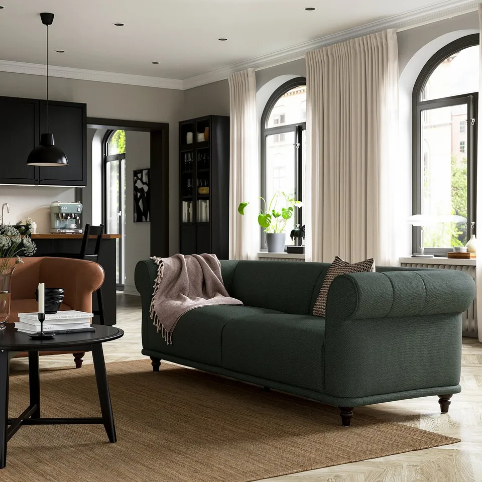 Cosy living room with a green VISKAFORS sofa, brown armchair, black coffee table, and arched windows with curtains.
