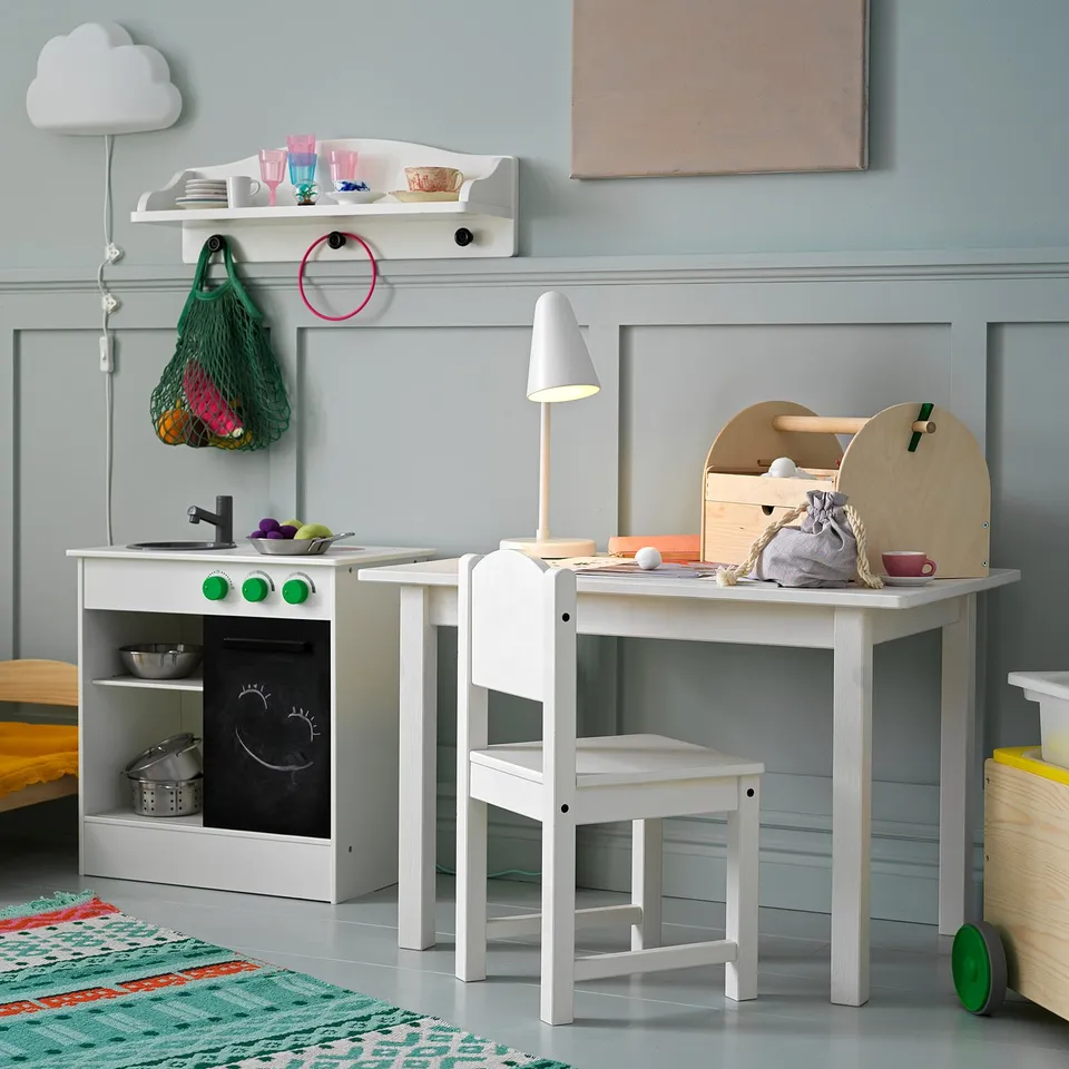 Playroom with white SUNDVIK table, chair, and toy kitchen. Blue walls, colourful toys, and green rug.