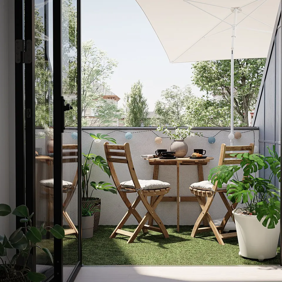 Modern balcony with green RUNNEN grass, wooden chairs, and plants. Large window and white umbrella.