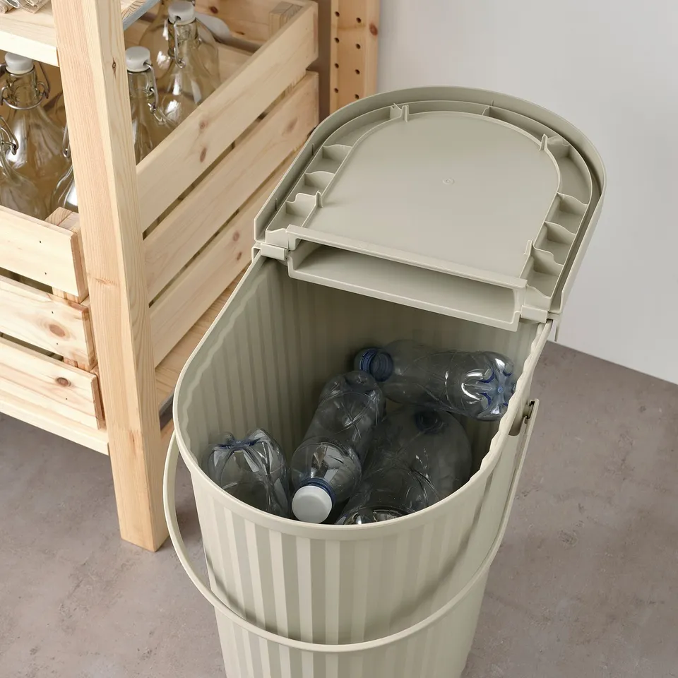 Recycling bin with lid holds plastic bottles, great for sorting home waste.