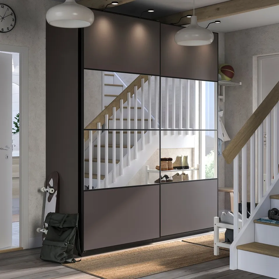 Modern entryway with mirrored & wooden sliding door, white staircase, grey backpack, and hanging lights.