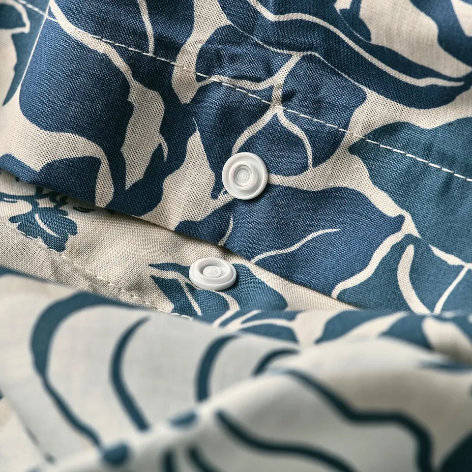 Close-up of a duvet cover with blue leafy pattern, showing press-stud fastener.