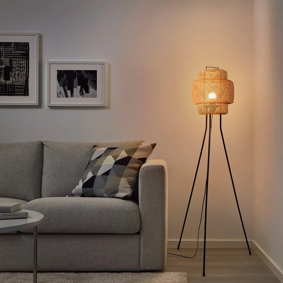 Floor lamp next to sofa, bamboo shade, warm light, three black legs, cosy ambiance.
