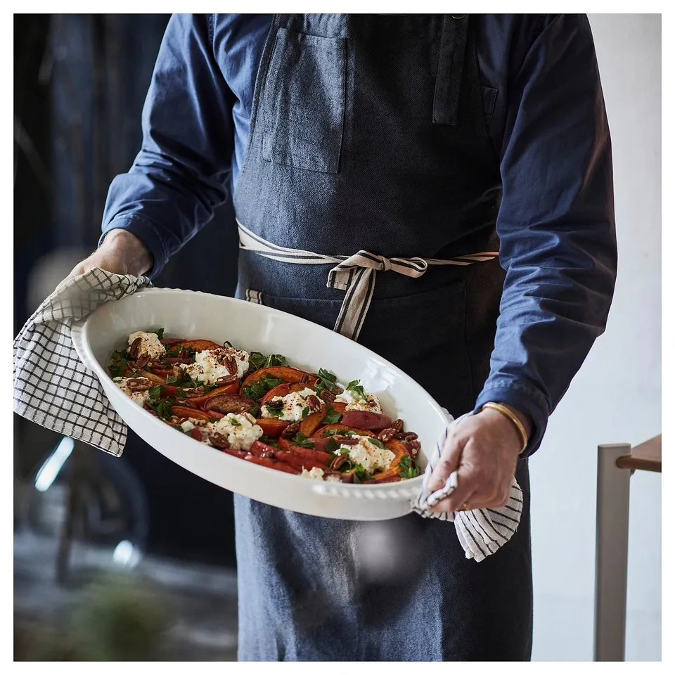 Person holding roasted veg & cheese dish, wearing apron.
