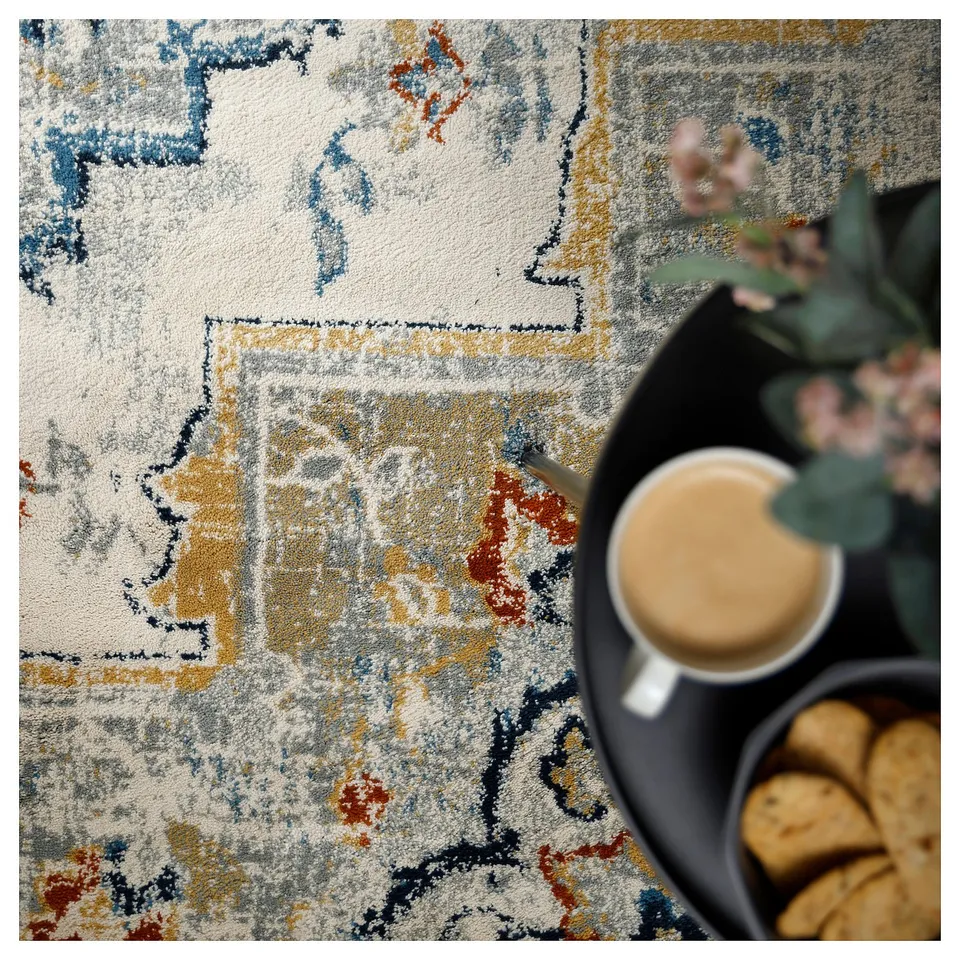 Abstact rug with yellow, blue, and red patterns. Nearby modern tray with coffee and cookies.