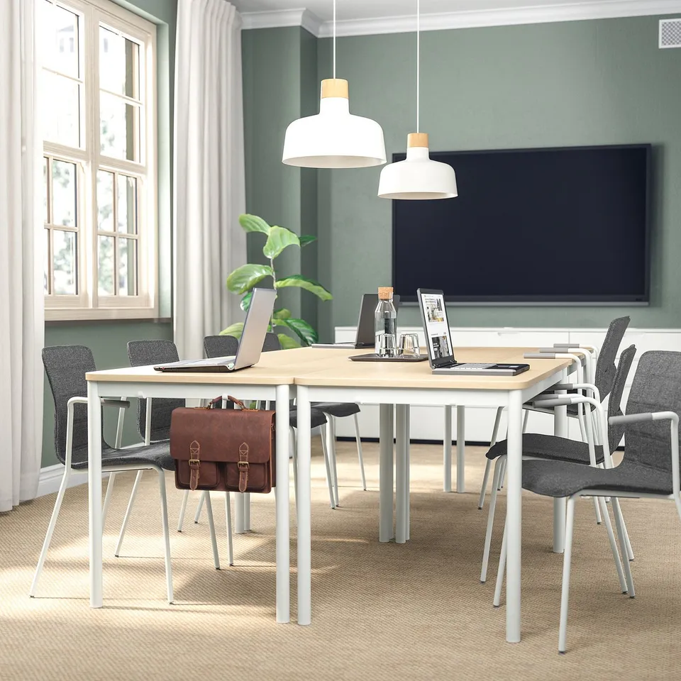 Modern office setup with wooden table, six grey chairs, tv, two pendant lights, and a plant.