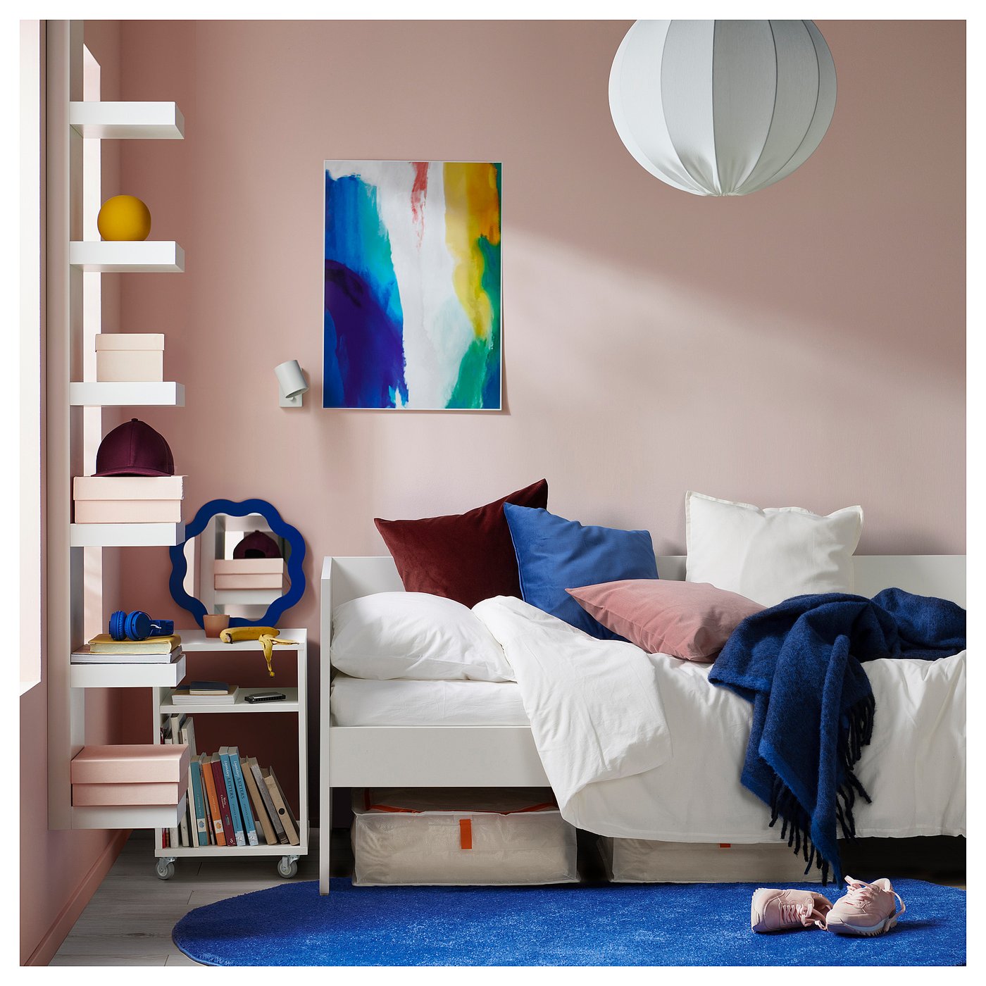 Cosy bedroom with white VIHALS daybed, colourful pillows, blue rug, pink walls, wall art, and hanging lamp.
