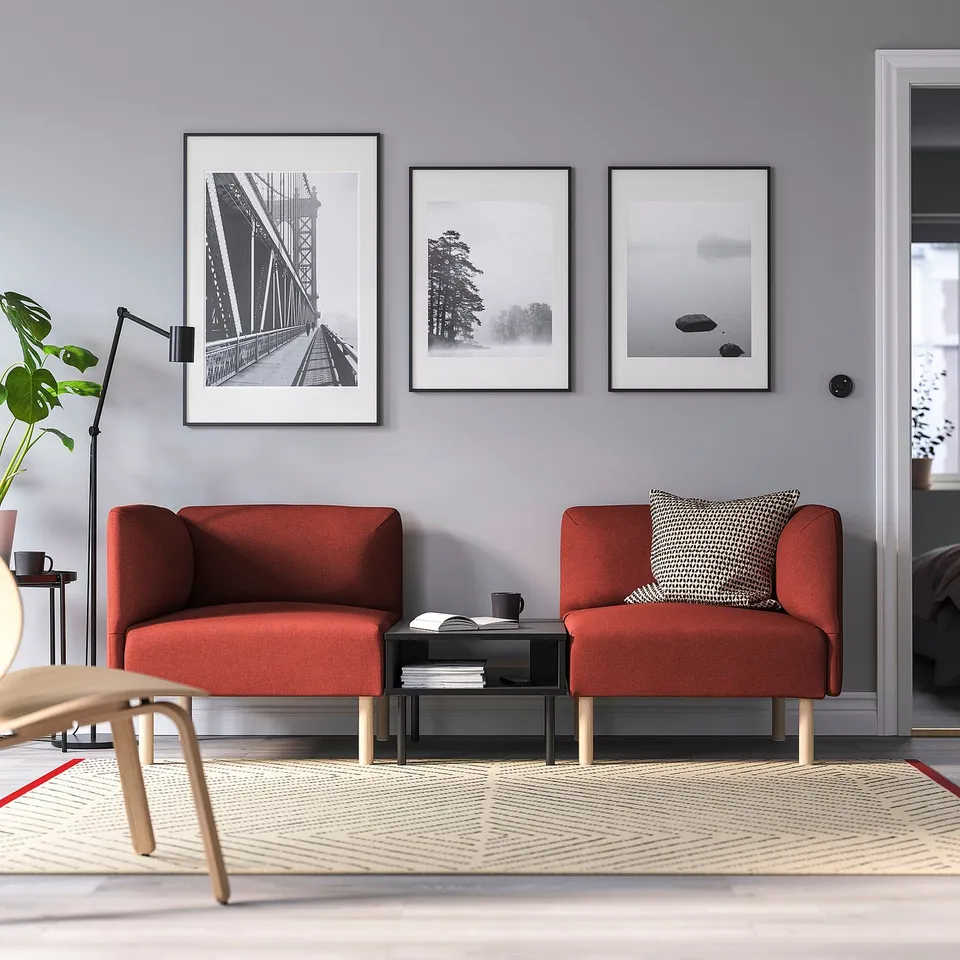 Modern living room with grey walls, red sofas, black table, geometric rug, and art.