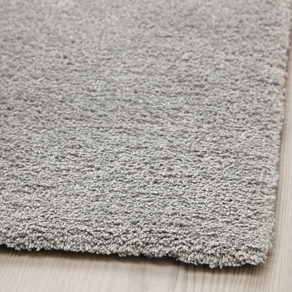 Close-up of soft, light grey rug with textured, shiny surface, placed on wooden floor.
