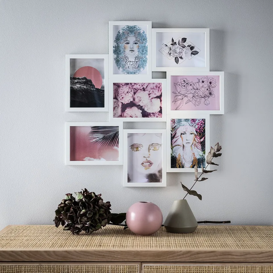 Wall art display with six framed pictures in white, featuring floral and face designs. Below it, a shelf holds decorative vases and dried flowers.