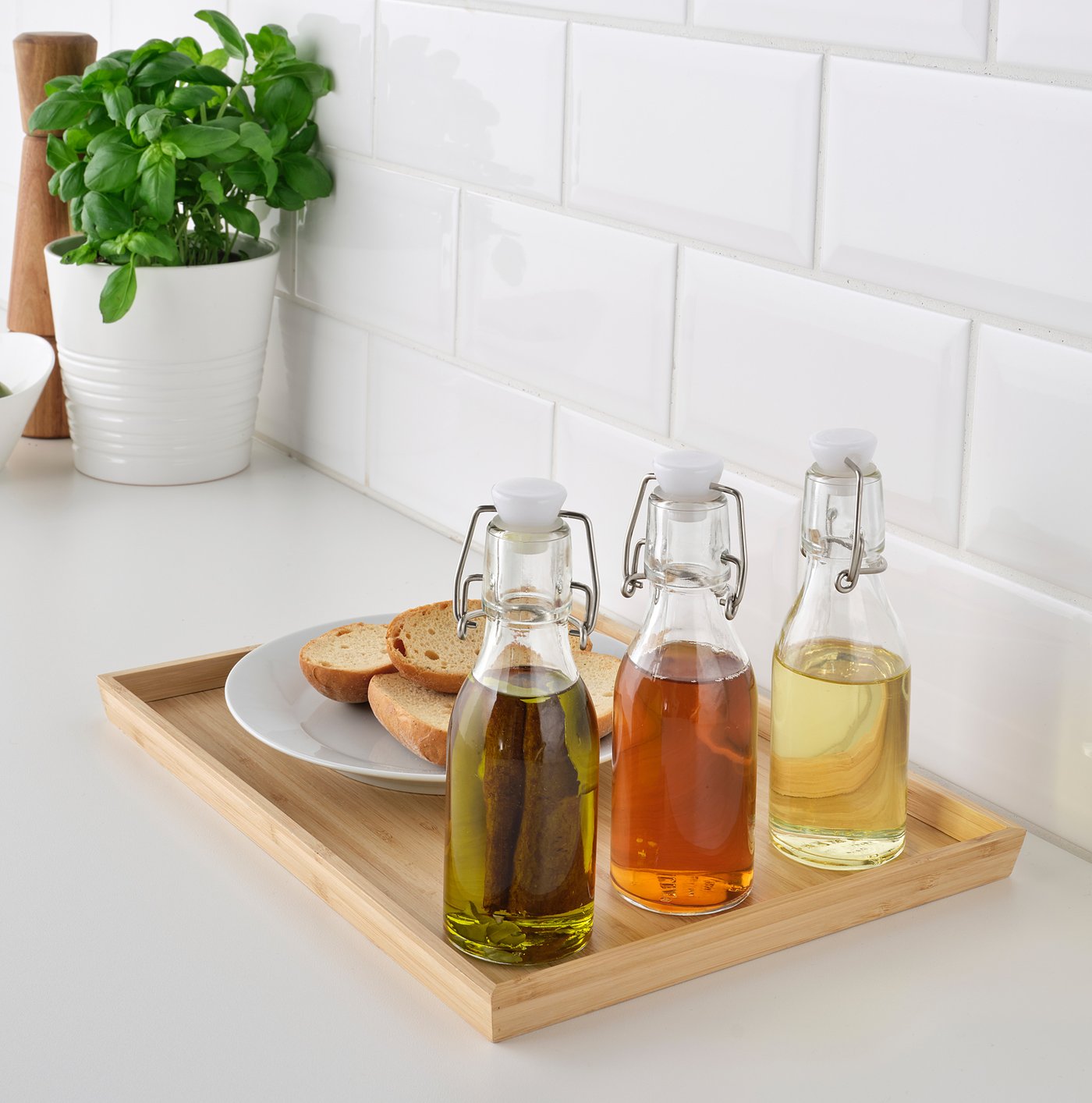Three glass bottles with stoppers on a tray beside bread and a plant.