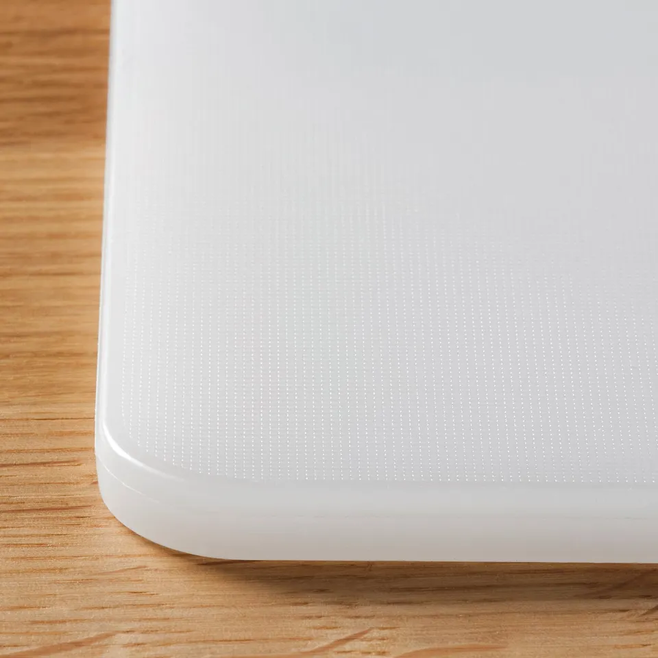 Close-up of a white plastic chopping board on a wooden surface, showcasing its smooth texture and durability.