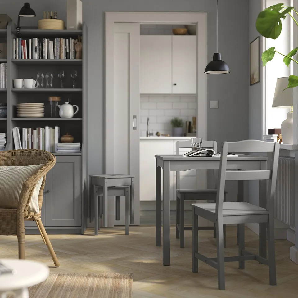 Small grey dining set in kitchen with table and two chairs, wooden, modern design, positioned near a grey bookshelf.