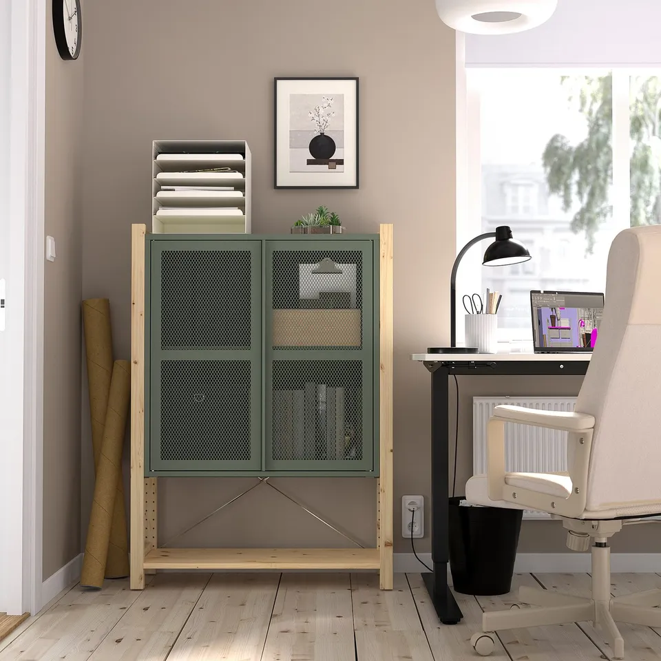 Home office IVAR side unit in natural wood, tall with mesh doors, positioned beside a desk with a laptop, chair, and lamp.
