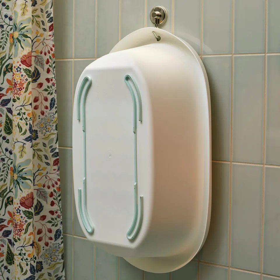 White baby bath with teal handles hangs on wall tile, soft edges, anti-slip bottom.